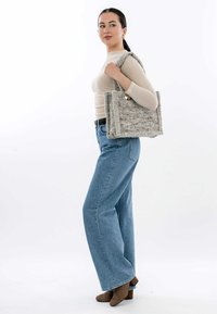 Borsa tote grigia con una superficie texturizzata, di forma rettangolare, caratterizzata da una finitura morbida e da un manico liscio in contrasto. Indossata sopra una maglietta beige e jeans blu.
