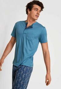Teal T-shirt met korte mouwen, voorzien van een kraag met knopen en een zak, gecombineerd met marineblauwe pyjamabroek met een patroon en bloemenaccenten.