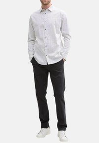 Chemise blanche à manches longues avec un motif géométrique noir, assortie à un pantalon noir et des baskets blanches. Détails de boutons sur le devant de la chemise.