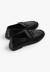 Mocasines de cuero negro con una superficie lisa, punta redondeada y costuras decorativas a lo largo del borde, con una suela de goma plana.