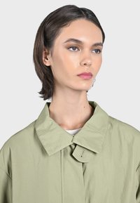 Ljusgrön oversized jacka med en stor krage och knappstängning. Har en mjuk textur och minimalistisk design.