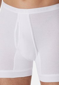 White ribbed boxer briefs with a smooth elastic waistband featuring the "Schiesser" logo. Made of soft fabric, designed for comfort and fit.