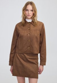 Chaqueta recortada de imitación cuero marrón con cierre de botón y un patrón texturizado, combinada con una falda mini texturizada a juego.