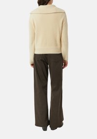 Kremowy, teksturowany kardigan z szerokim kołnierzem, długimi rękawami i krótkim fasonem, zestawiony z ciemnymi spodniami o szerokich nogawkach.