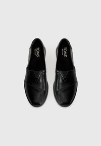 Fekete bőr slip-on cipő, lekerekített orral, varrott díszítésekkel és logóval a talpbetéten. Simaság és letisztult dizájn jellemzi.