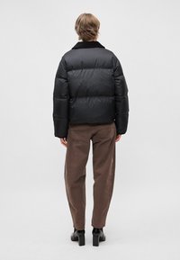 Črna puhovka z zaobljenim ovratnikom, prešita zasnova in subtilen lesk, v kombinaciji s rjavimi hlačami in črnimi škornji s peto.