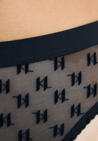 Zwarte lingerie met een gladde tailleband en een doorschijnend mesh lichaam, met een subtiel patroon van herhaalde contrasterende letters. Gelaagde randen.