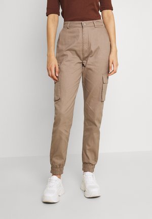 Pantalon cargo marron avec des poignets élastiques, des passants de ceinture, des poches latérales et une fermeture à bouton, associé à des baskets blanches.