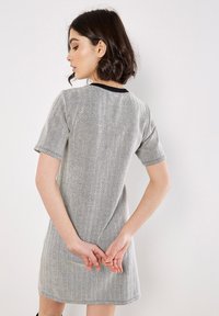 Sukienka w szary wzór houndstooth z krótkimi rękawami i czarnym kołnierzykiem. Materiał wydaje się teksturowany, o luźnej, dopasowanej sylwetce.