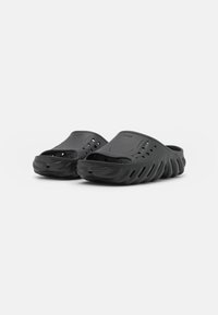 Crne slip-on klompe izrađene od laganog materijala, sa zaobljenim oblikom, perforiranim dizajnom i teksturiranom podlogom za bolje prianjanje.