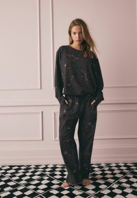 Set di pigiami nero accogliente con stampa leopardata e dettagli rosa, composto da una maglia a maniche lunghe a taglio ampio e pantaloni con vita elastica coordinati.