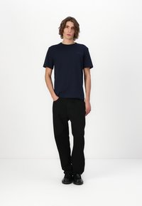 Camiseta de manga corta de color marino, de material de algodón, corte relajado, combinada con pantalones de pierna ancha negros y zapatos negros, de pie sobre un fondo blanco.