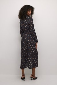 Marineblaue Pünktchenkleid mit langen Ärmeln, taillierter Taille und rocklanger Skirt. Hergestellt aus leichtem, leicht glänzendem Stoff.