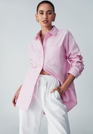 Light pink button-up shirt with a chest pocket, rolled sleeves, and a relaxed fit, paired with white, drawstring waist pants.