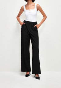 Pantalons larges noirs avec poches avant, assortis à un haut sans manches blanc avec un décolleté en scoop et un petit détail en forme de trou de serrure.