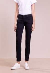 Svarta jeans i denim med en figurnära design, femfickorsstil och en slät textur, kombinerade med en vit t-shirt och vita sneakers.