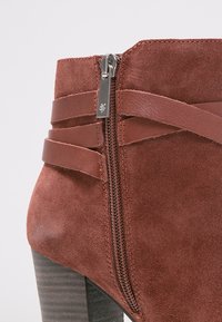 Stivaletto in suede marrone con cerniera laterale e dettagli in pelle incrociati, dotato di tacco a blocco e superficie texturizzata.