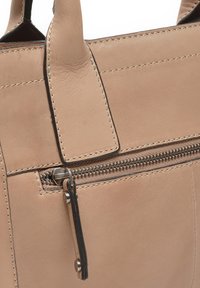 Lichtbeige leren handtas met een textuur oppervlak, contrasterende stiksels en een ritszak met een metalen rits.