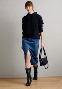 Sweatshirt à capuche noir, jupe crayon en denim avec fente sur le côté, bottes noires jusqu'aux genoux et un petit sac à main noir. Design simple et moderne.