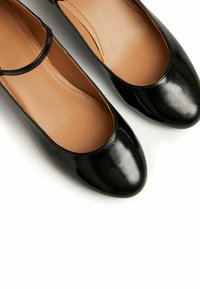 Zapatos planos de charol negro con punta redonda, que cuentan con una correa central en el empeine y un forro interior suave.