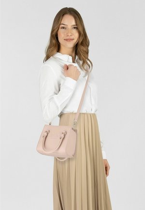 Pequeño bolso rosa con dos asas y una correa larga ajustable, cuenta con un logo en relieve y textura de cuero suave. El modelo lleva una camisa blanca.