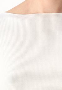 Λευκό ριγωτό ύφασμα με λεία υφή, με πλατύ, επίπεδο λαιμόκομμα και εφαρμοστή γραμμή, που τονίζει έναν μινιμαλιστικό σχεδιασμό.