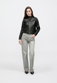 Μαύρο δερμάτινο μπουφάν bomber με φερμουάρ μπροστά, δύο τσέπες στο στήθος και ριμπ τελείωμα, συνδυασμένο με γκρι τζιν ψηλόμεσο και μαύρα μυτερά παπούτσια.