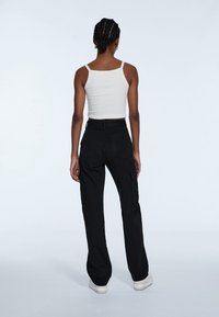 Schwarze Cargo-Hose mit Seitentaschen, hoher Taille und lockerer Passform, kombiniert mit einem taillierten weißen Tanktop. Glattes Baumwollmaterial.