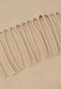 Beige ullskjerf med en myk tekstur, med en frynsekant med tvunnet garn langs den ene kanten.