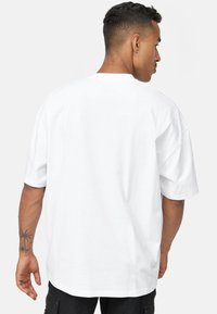 Camiseta blanca de gran tamaño con mangas cortas y cuello redondo, hecha de algodón. Presenta un diseño sencillo sin logotipos ni patrones visibles.