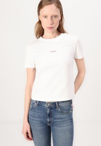 Bijela pamučna majica s okruglim izrezom i kratkim rukavima, sa malim crvenim izvezenim "Calvin Klein" logotipom na prsima.
