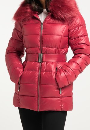 Woman wearing a red quilted puffer jacket with zipped pockets, a belted waist, and a large faux fur collar, hands in pockets.