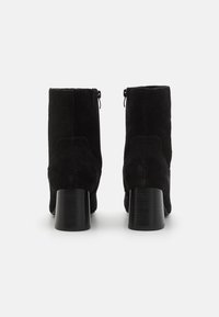 Bottes de cheville en suéde noir avec un bout arrondi, deux fermetures éclair à l'arrière et un talon épais noir. La texture semble douce et lisse.