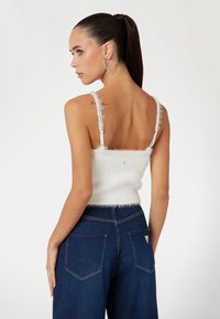White fuzzy knit top with thin straps. Paired with dark blue high-waisted jeans featuring visible pockets and stitching details.