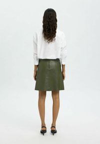 Zielona skórzana spódnica w kształcie litery A z szwem z tyłu. Połączona z białą koszulą na guziki i czarnymi butami na obcasie.