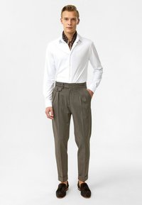 Witte langpoloshirt met een button-down kraag, gecombineerd met grijze, gestreepte broek met een zijaanpassing en manchetten. Donkere schoenen maken de outfit compleet.
