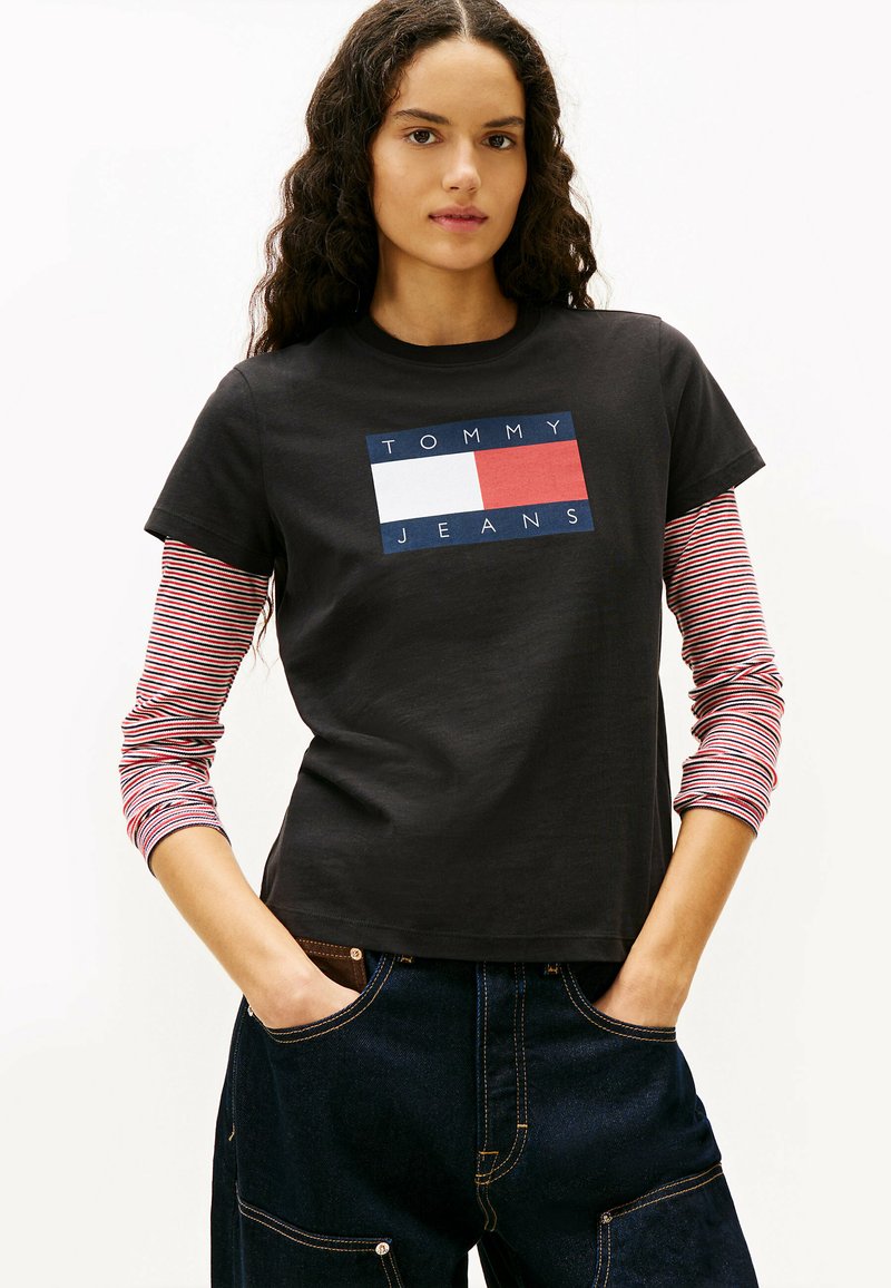 Czarna bawełniana koszulka z niebieskim, białym i czerwonym prostokątnym logo z napisem "TOMMY JEANS." Długie rękawy w czerwono-białe paski widoczne spod spodu.