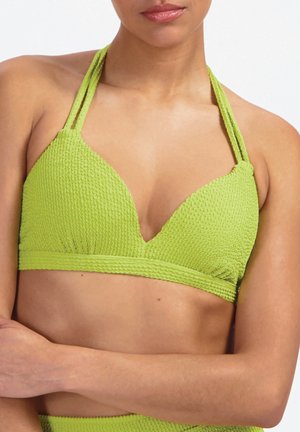 Kobieta w teksturowanym, limonkowo-zielonym bikini na szyję, widoczna od ramion do pasa, ze skrzyżowanymi ramionami na białym tle.