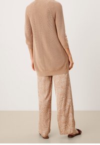 Lång beige stickad tröja med trekvartslånga ärmar, parat med vida byxor med ett ljusbrunt bladmönster. Slät textur, avslappnad passform.