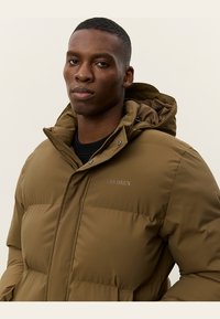 Chaqueta acolchada marrón con cierre de cremallera, capucha con cordón y detalle de logo. Presenta un diseño elegante y una textura lisa y mate.