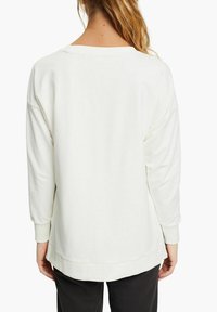 Sudadera blanca de gran tamaño con escote redondeado, mangas largas y puños acanalados. Textura suave y ajuste relajado, el dobladillo se extiende ligeramente en la parte trasera.