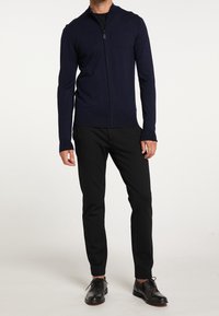 Navy zip-up sweater with a stand collar, fitted long sleeves, and ribbed hem. Paired with black trousers and black dress shoes.