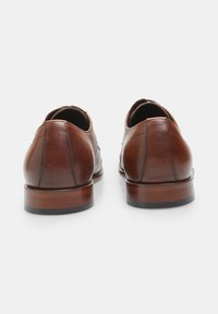 Scarpe da cerimonia in pelle marrone con una texture liscia, punta rotonda e tacco curvato, dotate di una suola in legno e dettagli di cucitura minimal.