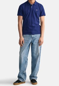 Navy blue polo shirt, short sleeves, with a small logo on the chest. Paired with light blue wide-leg jeans and black sneakers.