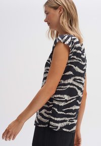 Camicia corta a maniche nere e bianche con un motivo astratto a onde orizzontali, tessuto morbido, vestibilità ampia e scollo rotondo.