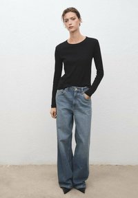 Zwarte lange mouwen top gecombineerd met lichtblauwe wijde jeans. De jeans hebben een hoge taille, subtiele stiksels en een ontspannen pasvorm.