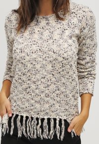 Pull en tricot beige avec motifs tachetés, manches longues et ourlet effiloché. Tissu texturé avec une coupe ample et décontractée.