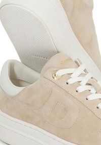 Beige suede sneakers with white rubber sole, flat laces, and gold accent logo. Textured surface with smooth white heel detail.