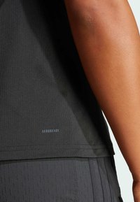 Zwarte sportshirt van rekbaar materiaal. Heeft een lichte glans, het "AEROREADY"-logo in lichtblauw en een aansluitende pasvorm die het lichaam omarmt.