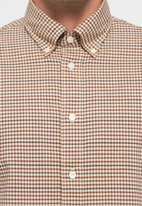 Collared button-up shirt with small checkered pattern in cream, brown, rust, and navy, shown from neck to mid-chest.